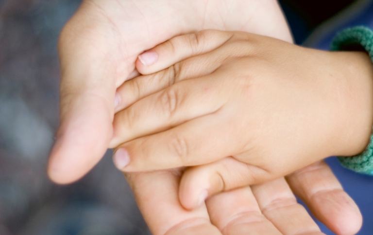 Ett barns hand som ligger i den öppna handflatan på en vuxen